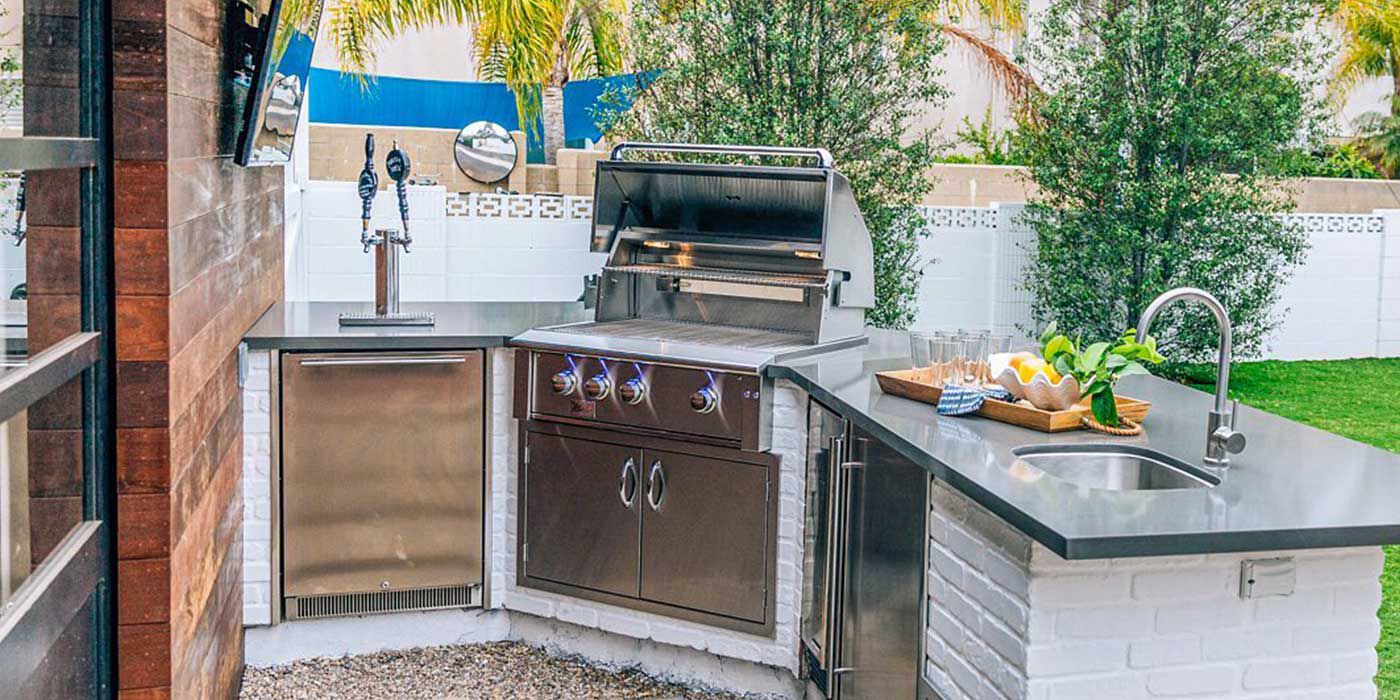 A small outdoor kitchen island with a white base, gray granite countertops, a stainless steel grill head, and an outdoor refrigerator, sink, and faucet.
