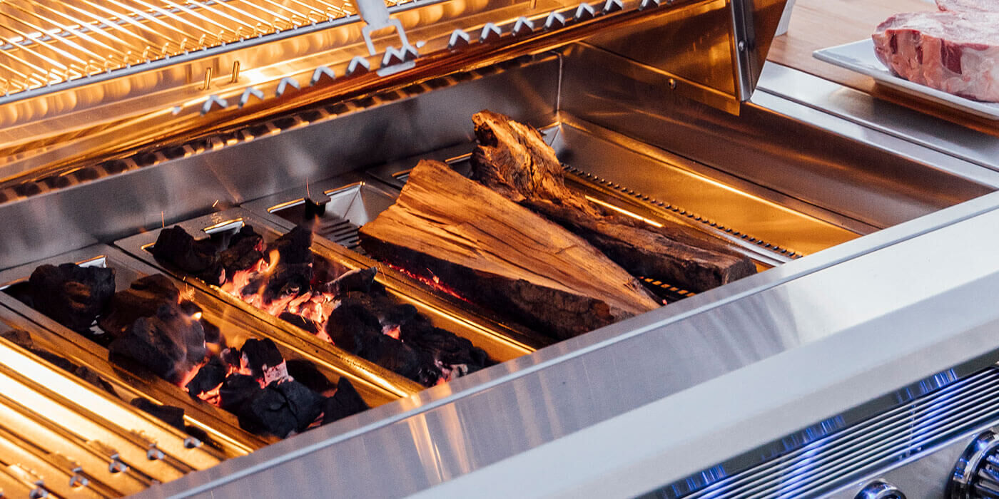 A close-up view of a stainless steel hybrid gas grill, loaded with infused wood for extra flavor.