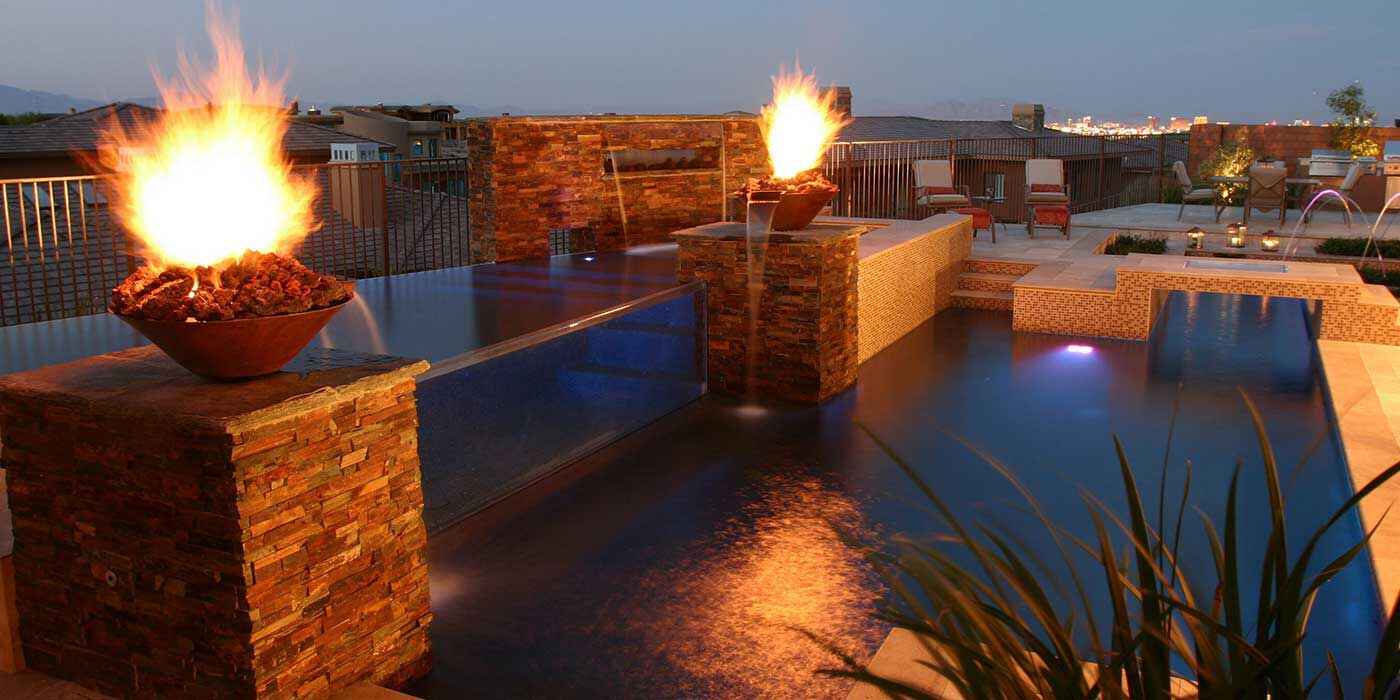 A large, outdoor pool with natural stone walls and two large copper fire and water bowls installed along the edge of the pool.