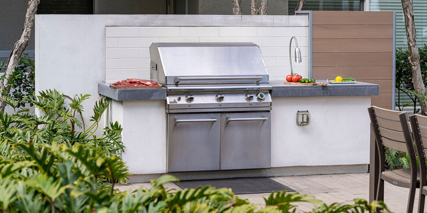A custom kitchen island with a white base, gray countertops, a built-in PGS grill,, and a stainless steel outdoor sink.