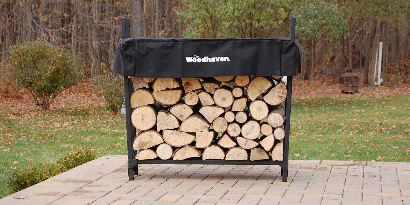 A black firewood rack with a matching black cover filled with seasoned wood logs.