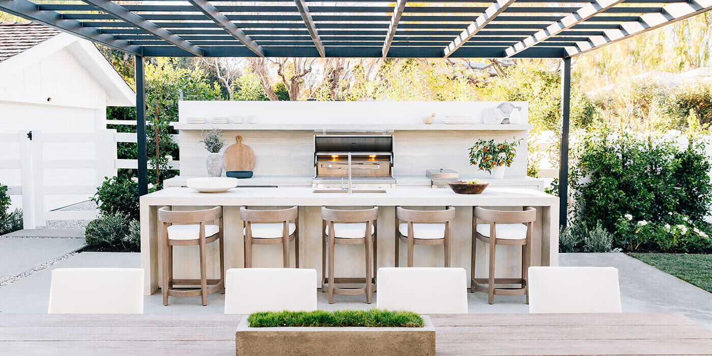 A custom outdoor kitchen and bar area with countertop seating, a large built-in grill, spacious white counters, an outdoor kitchen sink, and outdoor refrigerator.