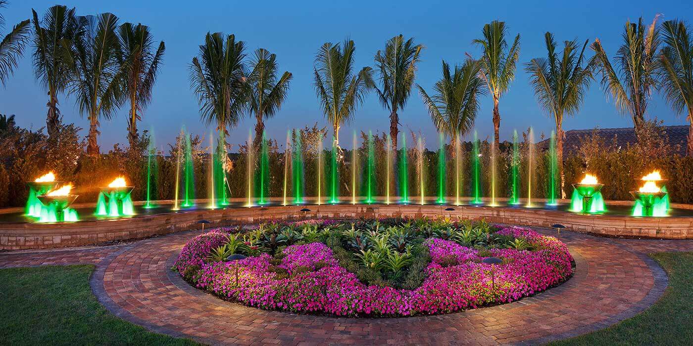Lely Resort in Florida view of water fountain lined with palm trees, illuminated jets of water, and fire and water bowls. 