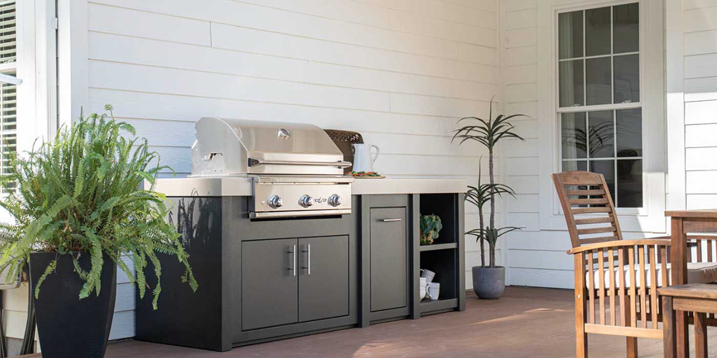 A small outdoor kitchen island with a stainless steel grill head, a refrigerator, and built-in storage drawers and doors. 