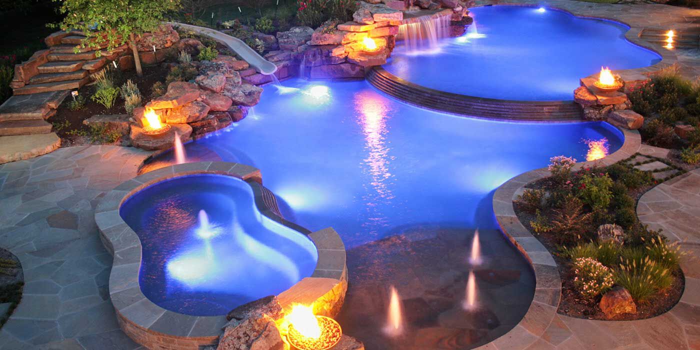 A large, organically shaped poolscape with several fire bowls, miniature backlit jets, and a waterfall.