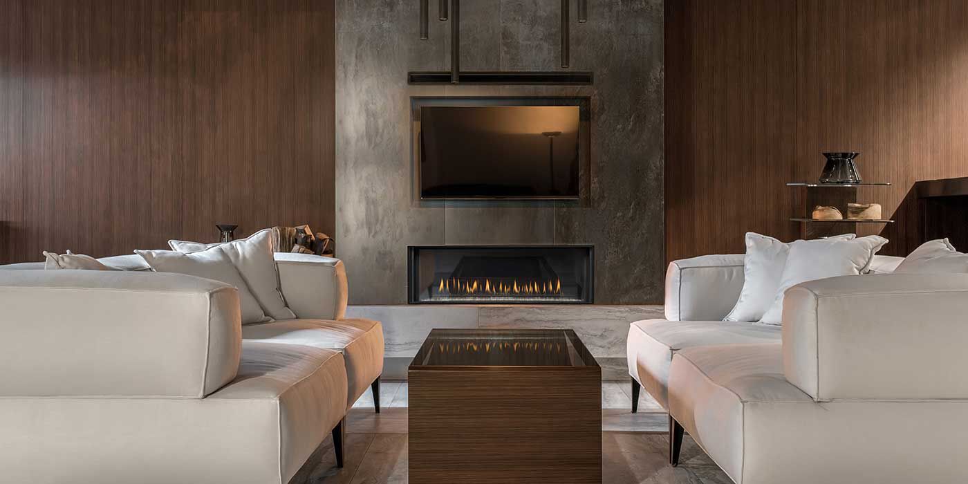 An industrial living space with custom wood plank finished walls, a large exposed cement hearth with a linear gas fireplace and a flatscreen TV, two large white couches, and a solid metal square coffee table.
