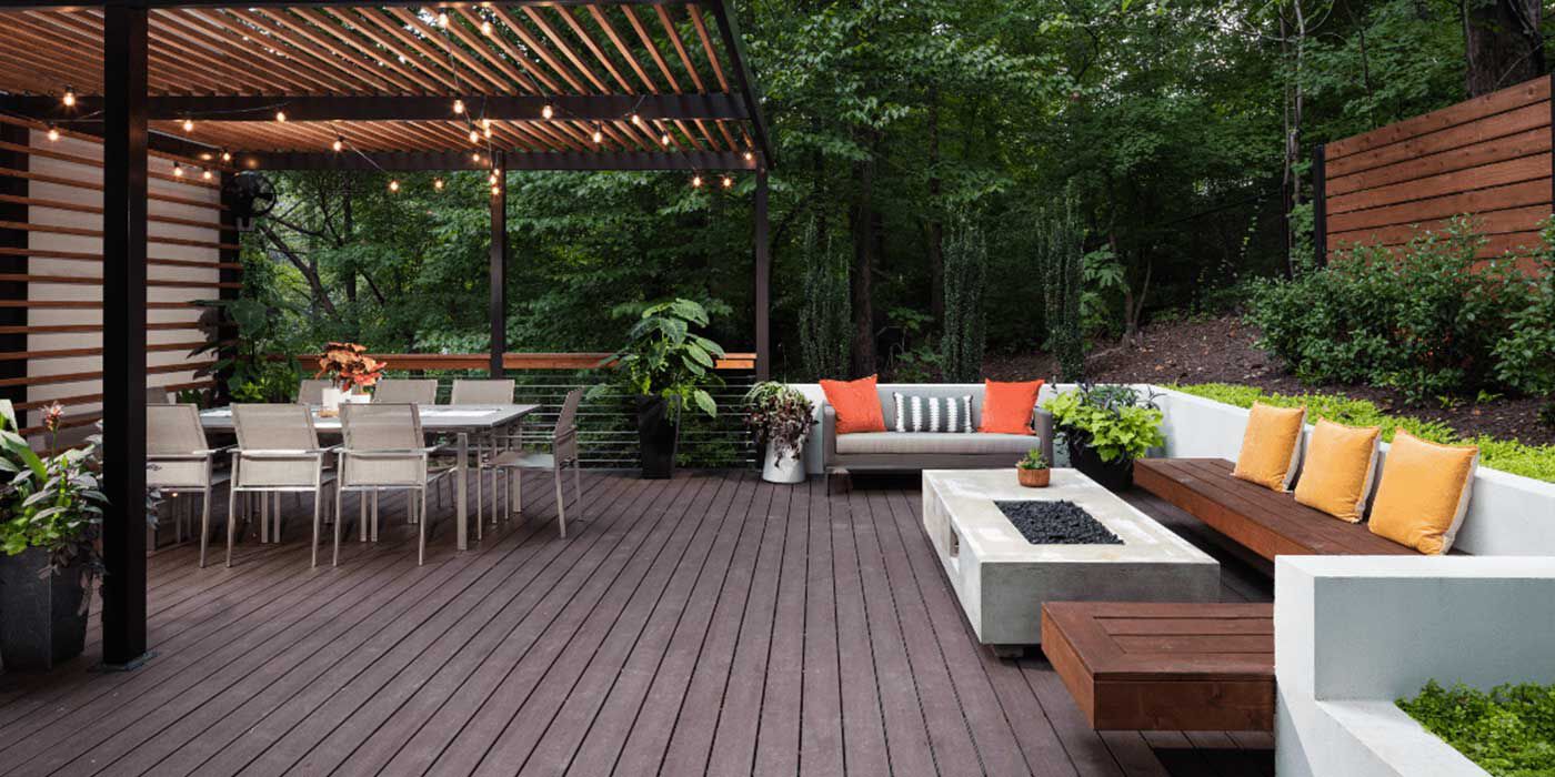 A large, contemporary backyard space with a wooden deck, wooden awning, dining area, an outdoor sitting area with a large white sectional couch and large, white linear gas fire pit