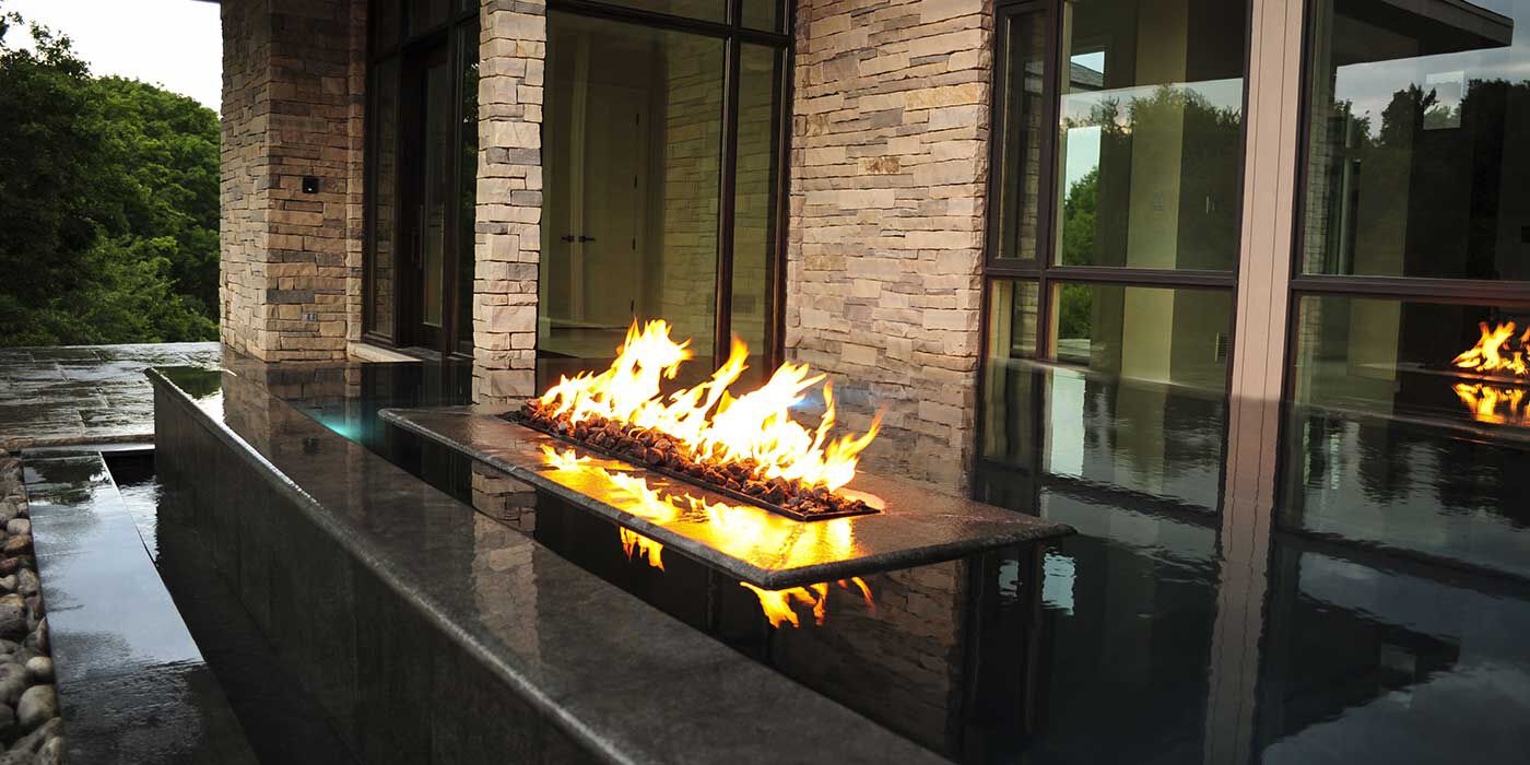 A large, linear black fire pit installed in the center of linear black water fountain.