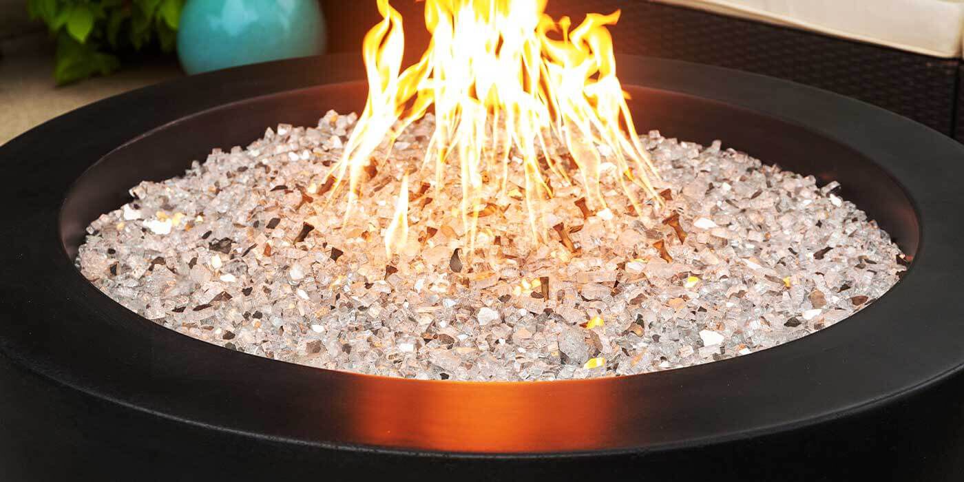 A round fire pit with burning flames and glass crystals inside a black metal frame.