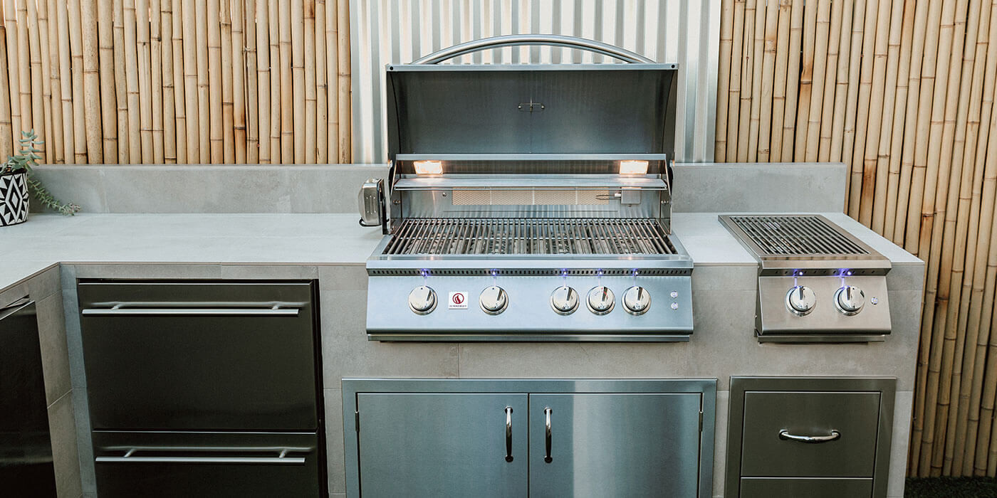A large, stainless steel gas grill head installed in a custom outdoor kitchen island with stainless steel storage doors and drawers.