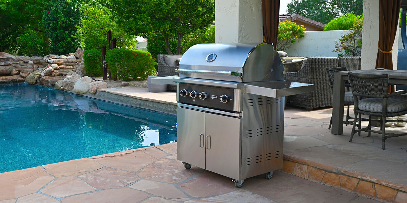 A stainless steel Wildfire gas grill cart on an outdoor patio near a large swimming pool.