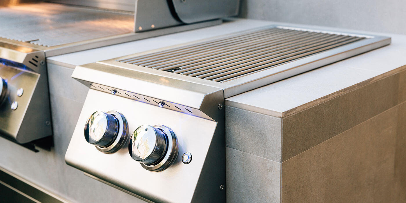 A stainless steel side burner with two temperature control knobs installed in a custom outdoor kitchen island.